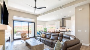A spacious living room with a large leather sectional sofa, a coffee table, and a TV mounted on the wall.