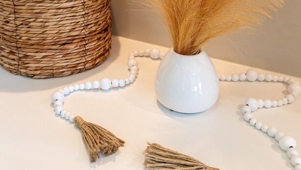 Un panier tressé contenant des plumes de jarre séchées et un vase blanc orné d’une guirlande de perles blanches.