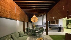 A modern living room with a wooden ceiling, a green sofa, a dining table with chairs, and a hanging light fixture. - CASA BALI - Charm and comfort in Guarajuba  (Guarajuba)
