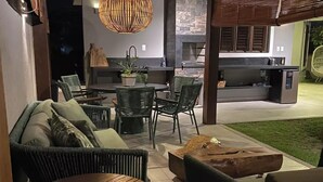 An outdoor patio area with wicker furniture, a round wooden table, and a hanging light fixture. - CASA BALI - Charm and comfort in Guarajuba  (Guarajuba)
