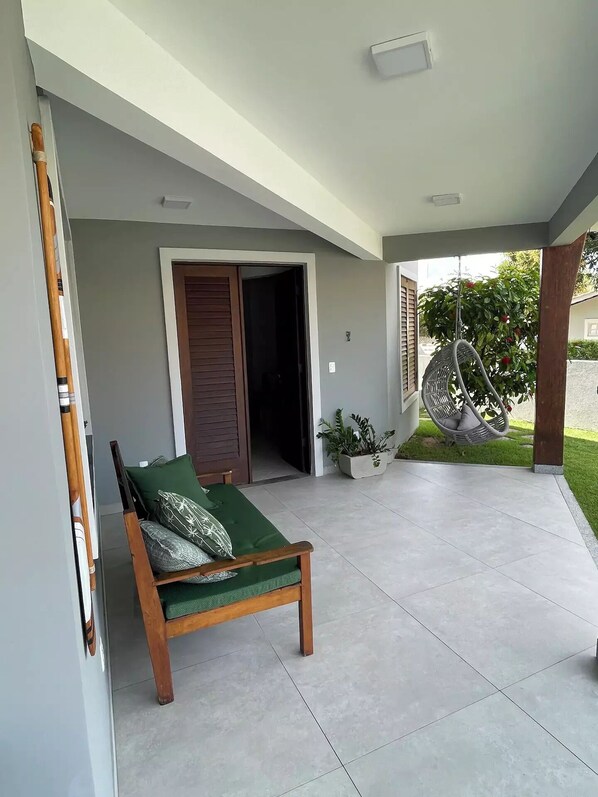 Quarto com sofá acolchoado verde, porta de madeira e cadeira suspensa.