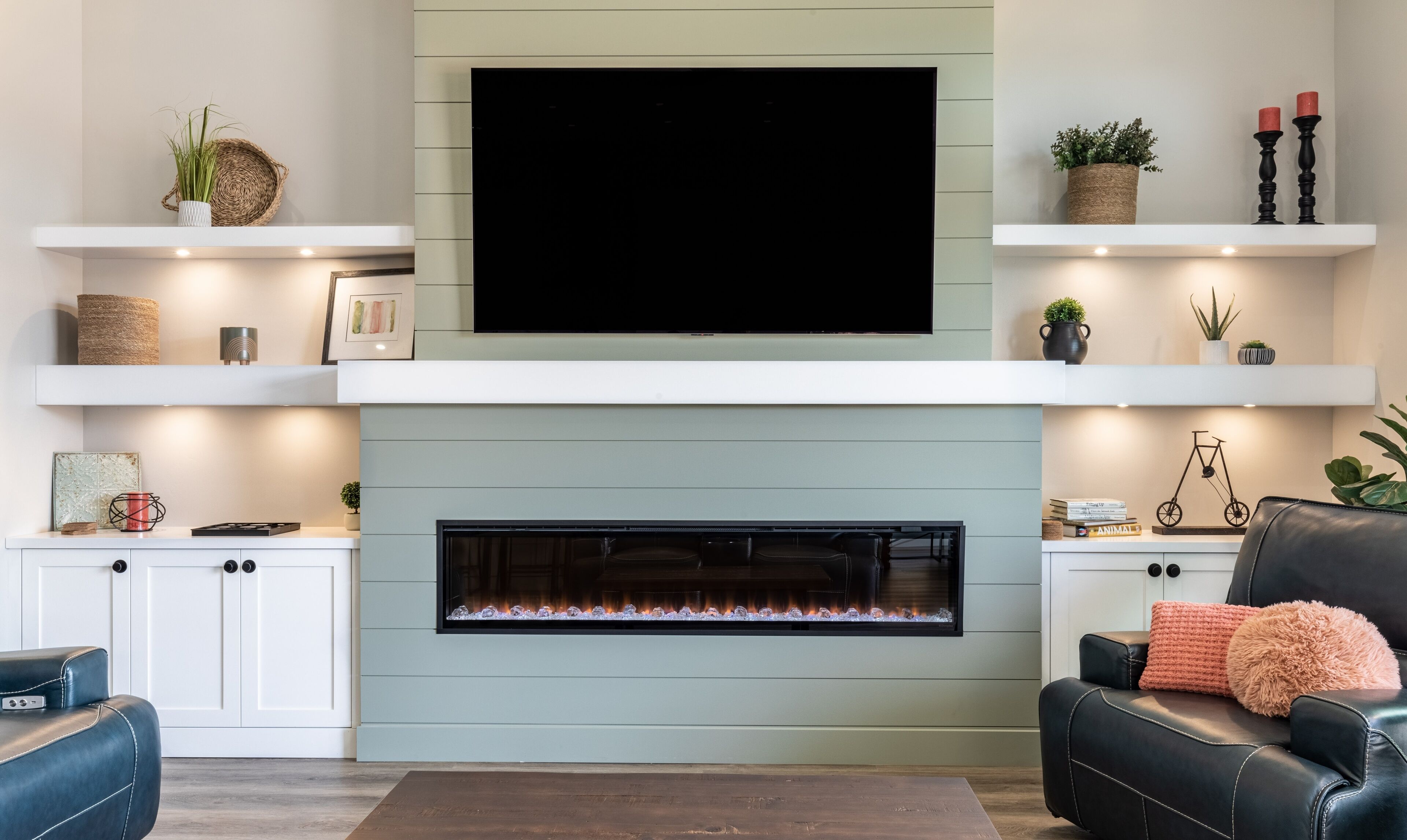 Uma sala de estar moderna com lareira, armários brancos, televisão montada e objetos decorativos nas prateleiras.