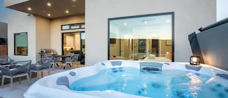 A modern outdoor hot tub area with seating and a glass-enclosed room in the background.