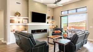 A modern living room with a fireplace, black leather sofa, and a dining area with a table and chairs. - Desert Dreaming 2 Bedroom Home by RedAwning (Washington)