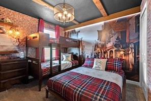 A themed hotel room with a brick wall, a mural, bunk beds, a desk, and a chandelier.