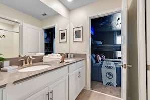 A modern bathroom with dual sinks, a large mirror, and a view into a bedroom with a bunk bed.