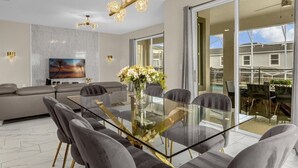 A modern dining area with a glass table, grey upholstered chairs, and a vase of flowers.