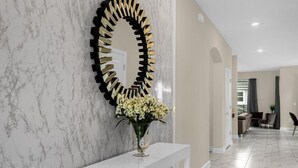A hallway with a marble wall, a decorative mirror, and a white console table with a vase of flowers.