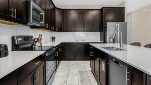 A modern kitchen with dark cabinetry, a white countertop, a stainless steel microwave, a built-in oven, and a dishwasher.