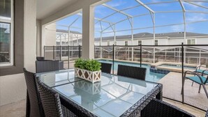 A glass-top table with wicker chairs and a potted plant, overlooking a swimming pool and residential buildings.