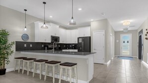 A modern kitchen with white cabinets, a central island with stools, pendant lighting, and a large clock on the wall. - 9 Bed Storey Lake Star Wars Dream Home 9 Bedroom Home by RedAwning (Kissimmee)