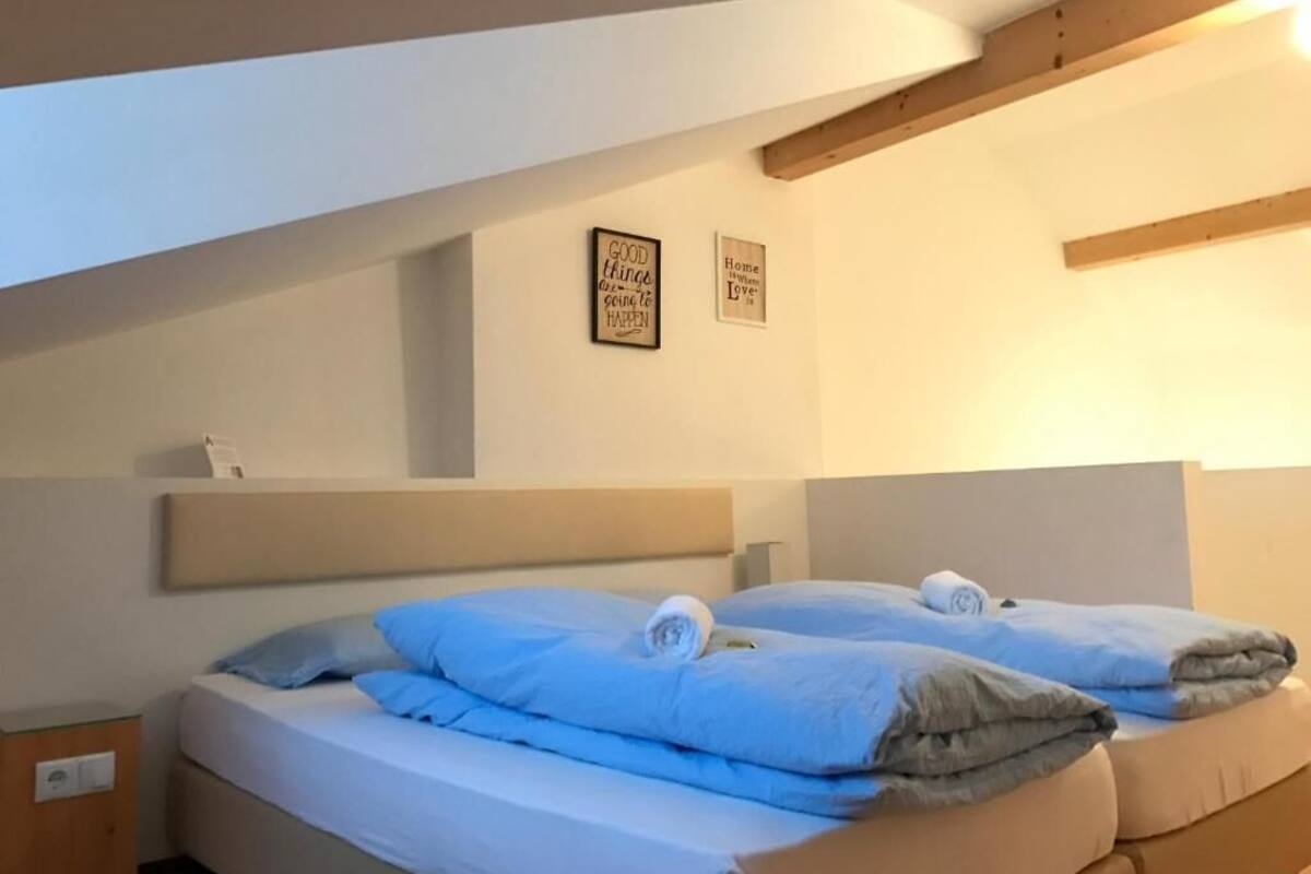 A bedroom with two beds, each with blue bedding and rolled towels. There are two wall-mounted signs with inspirational quotes.