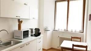 A compact kitchen with white cabinets, a microwave, a kettle, and a window with curtains. - Argentieri Guesthouse (Bolzano)