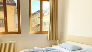 A hotel room with two beds, a window with curtains, a radiator, and a lamp. - Argentieri Guesthouse (Bolzano)