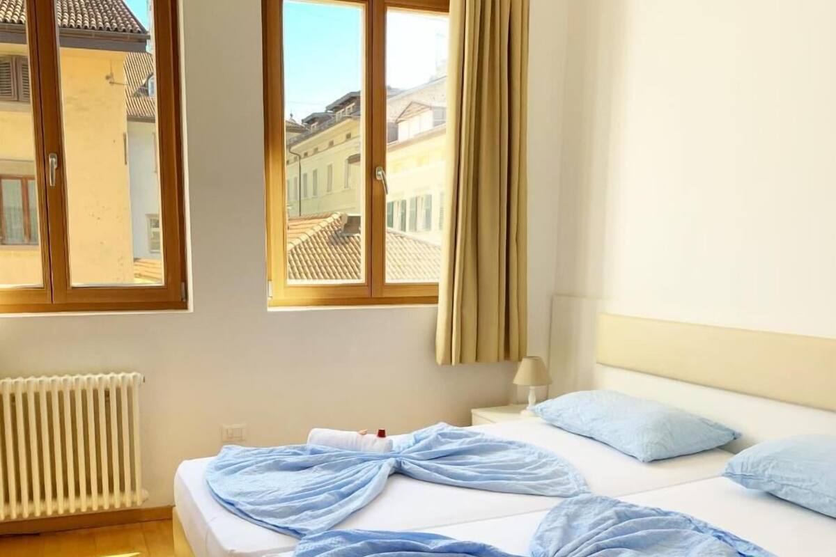 A hotel room with two beds, a window with curtains, a radiator, and a lamp.