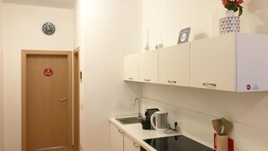 A small kitchen with a sink, a stove, and cabinets. There is a clock on the wall and a door with a number sign. - Argentieri Guesthouse (Bolzano)