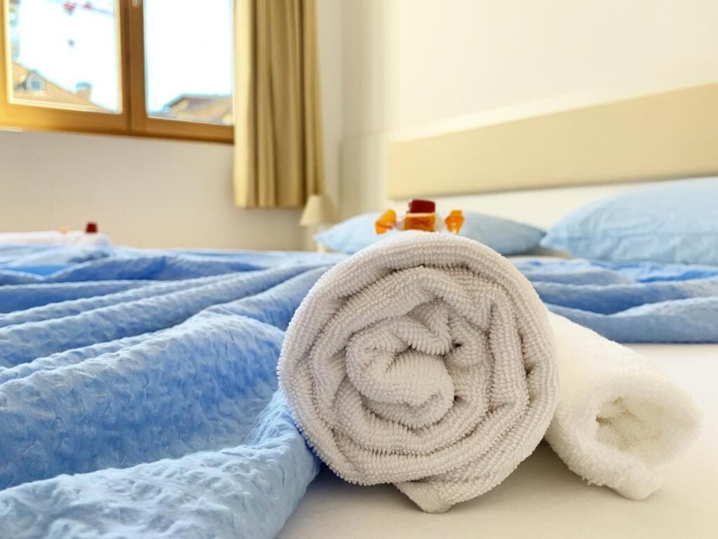 Una cama bien hecha con una manta azul y una toalla blanca enrollada.
