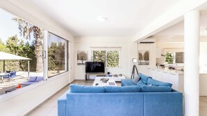 Ein modernes Wohnzimmer mit einem großen, blauen Sofa, einem Flachbildfernseher und einem Essbereich mit Tisch und Stühlen.