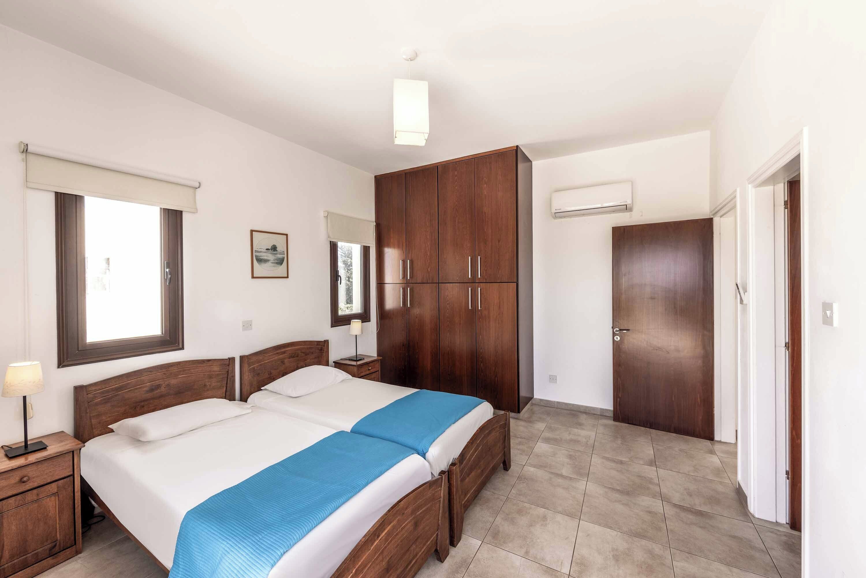 A bedroom with two beds, wooden wardrobe, and a window with a view.