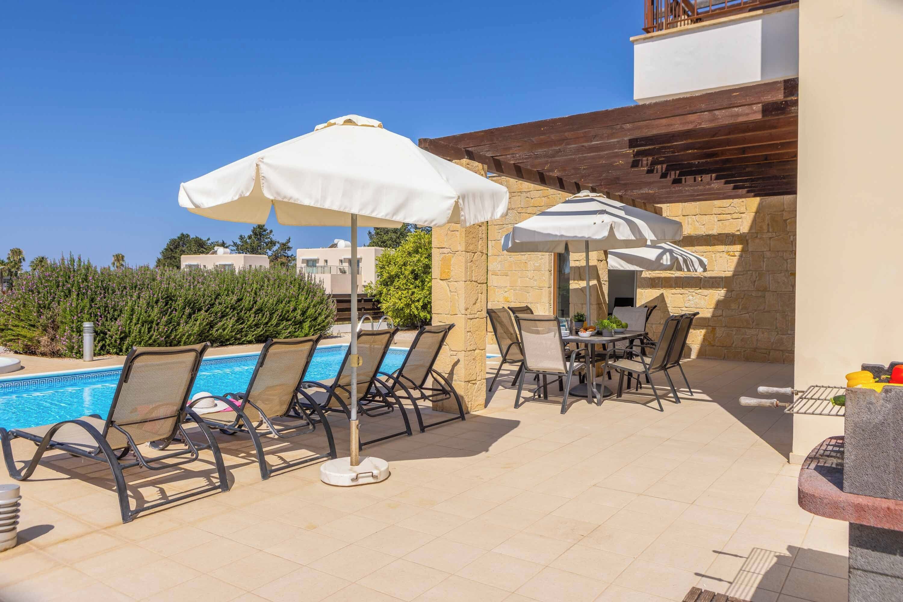 A poolside area with lounge chairs, umbrellas, and a barbecue grill.