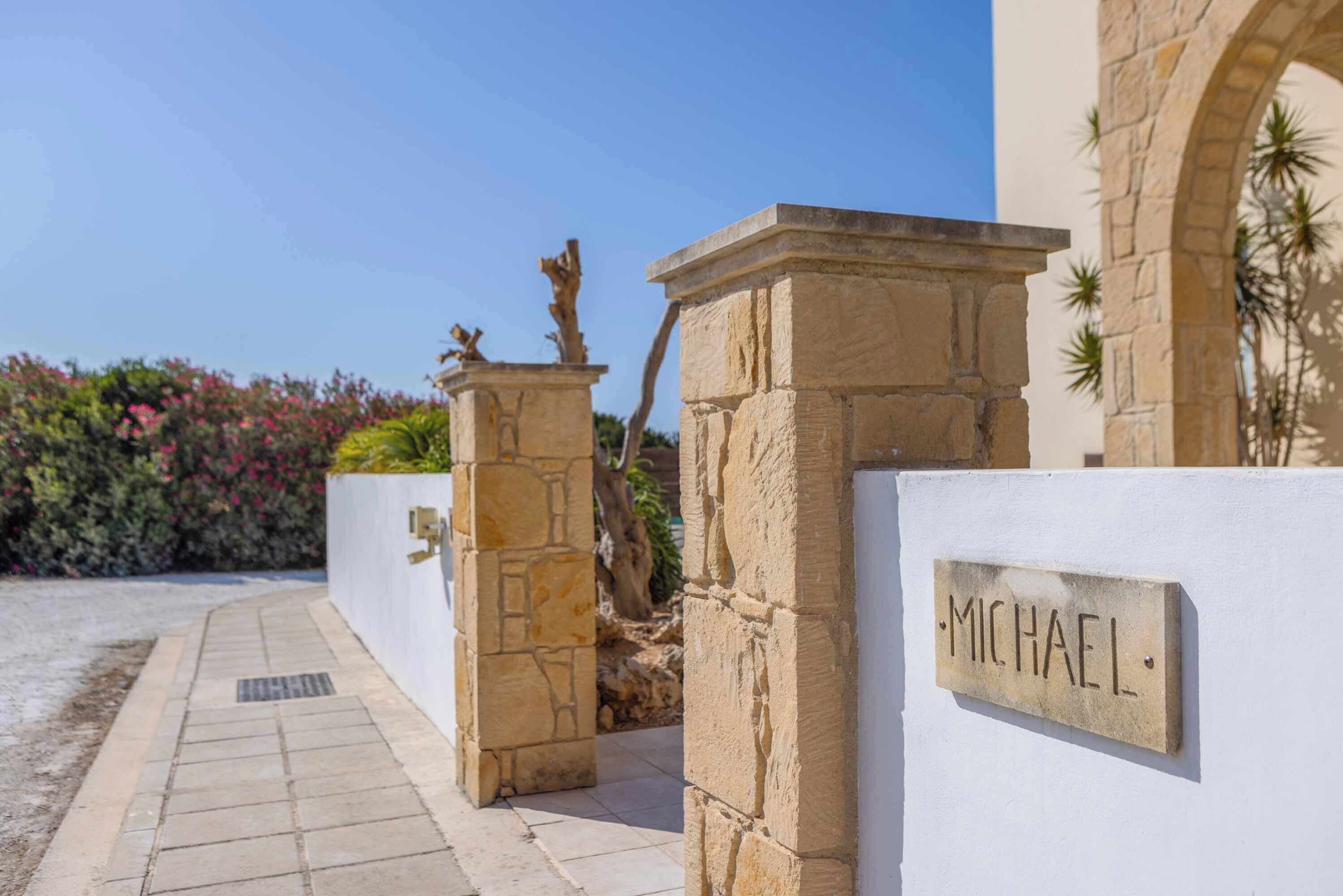 Une entrée en pierre surmontée d’une plaque portant le nom « MICHAEL » et un chemin menant à un bâtiment.
