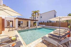 Ein Schwimmbad mit Liegestühlen, einer Pergola und einer überdachten Terrasse.