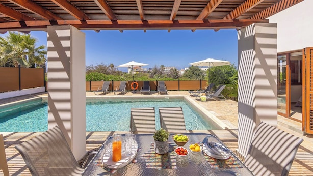 A poolside area with a table set for dining, lounge chairs, and umbrellas. - Coral Olympus Poseidon (Peyia)