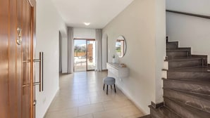 A hallway with a wooden door marked '3', a white vanity with a mirror, a small stool, and a staircase. - Coral Olympus Poseidon (Peyia)