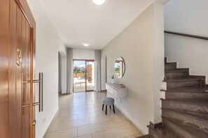 A hallway with a wooden door marked '3', a white vanity with a mirror, a small stool, and a staircase. - Coral Olympus Poseidon (Peyia)