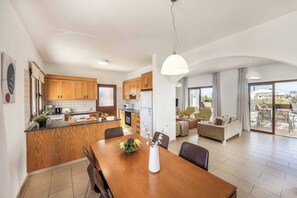 Eine moderne Küche mit Holzausstattung, ein Essbereich mit Holztisch und ein Wohnzimmer mit Sofa und Balkon.