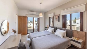 A modern bedroom with two beds, a desk, a mirror, and a view of the outside. - Coral Olympus Poseidon (Peyia)