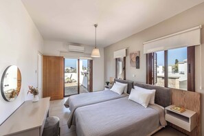 A modern bedroom with two beds, a desk, a mirror, and a view of the outside. - Coral Olympus Poseidon (Peyia)