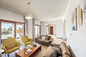 Ein modernes Wohnzimmer mit einer Couch, Sesseln, einem Couchtisch und Blick auf einen Pool.