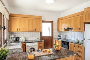 Eine moderne Küche mit Holzschränken, einem Spülbecken, einer Mikrowelle und einer Arbeitsplatte mit Obstschale und Zitrusfrüchten.