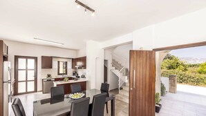 A modern kitchen with dark wood cabinets, a dining area with a glass table, and a view of a staircase leading to a balcony.