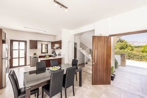 Eine moderne Küche mit dunklen Holzschränken, ein Essbereich mit Glastisch und Blick auf eine Treppe, die zu einem Balkon führt.
