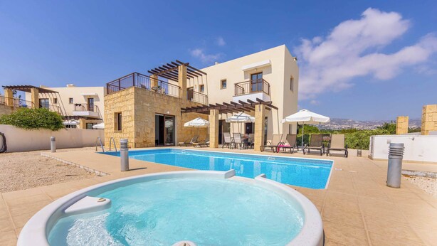 A swimming pool area with a hot tub, outdoor seating, and a view of a building with balconies.