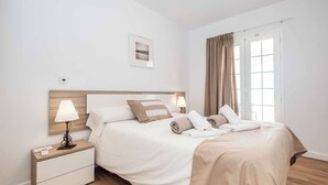 Un dormitorio ordenado con cama, mesitas de noche, una ventana con cortinas y un cuadro colgado en la pared.