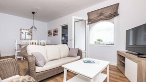 Una sala de estar moderna con un sofá, una mesita de centro blanca y un televisor sobre un mueble de madera.