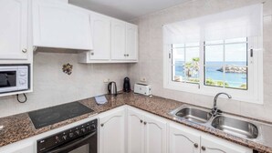 Una cocina con armarios blancos, encimera de granito, microondas integrado, tostadora y vista al mar a través de una ventana.