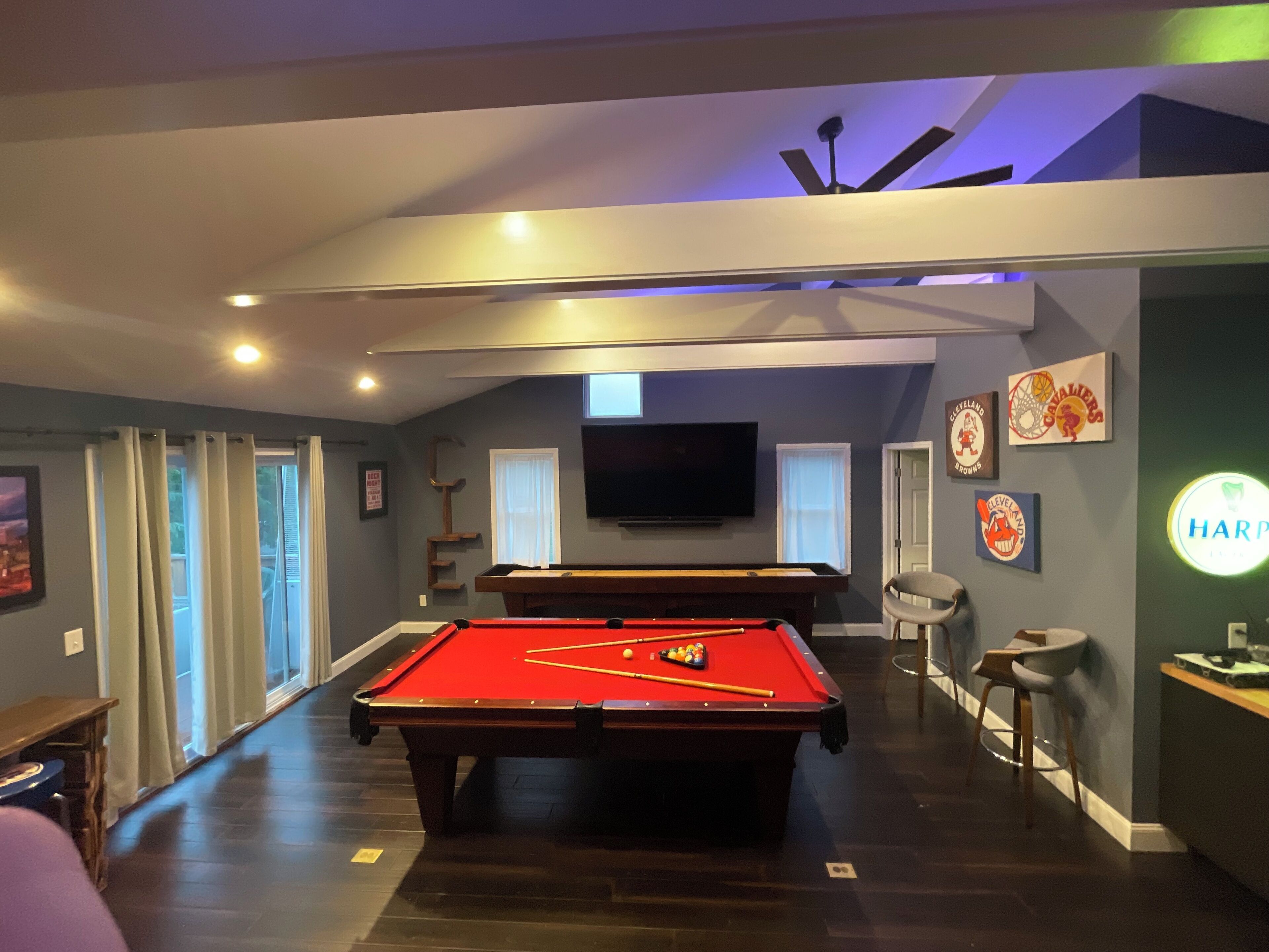 A pool table in a room with a ceiling fan, a TV mounted on the wall, and sports memorabilia.