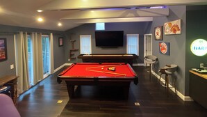 Une table de billard dans une pièce dotée d’un ventilateur de plafond, d’un téléviseur fixé au mur et de divers objets de collection sur le thème du sport.