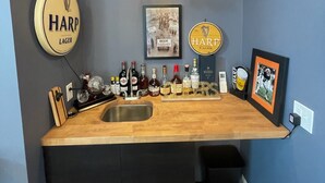 Un espace bar doté d’un comptoir en bois, d’un évier et d’un luminaire suspendu. On y trouve plusieurs robinets à bière et des bouteilles disposées sur le comptoir.