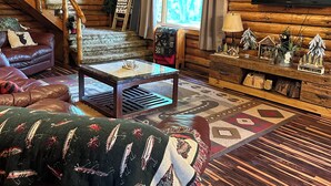 L’intérieur d’un chalet confortable, avec des murs en bois, un escalier en bois, un canapé en cuir et un téléviseur fixé au mur.