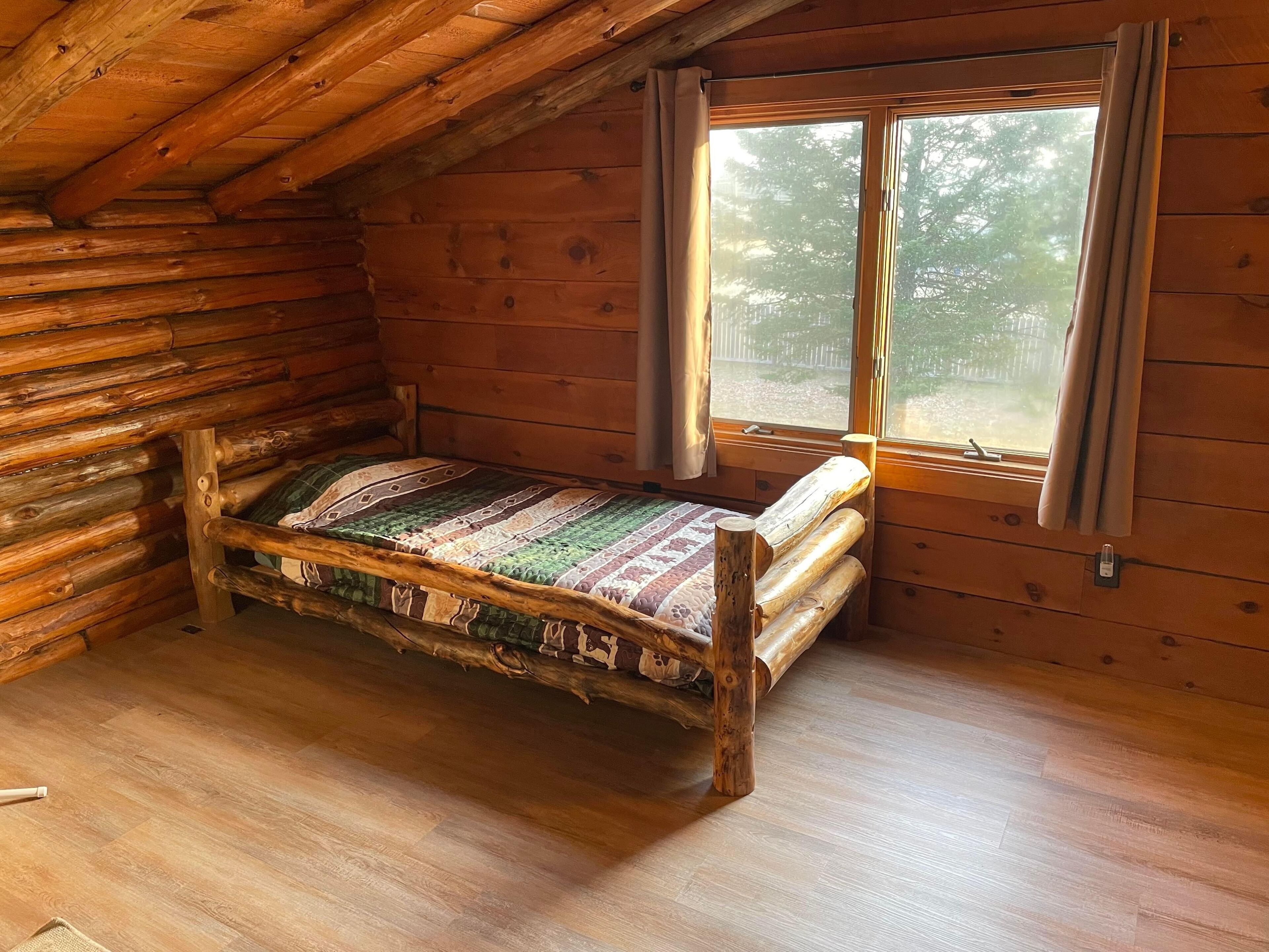Une chambre de style rustique, avec un lit en bois, une fenêtre avec des rideaux et un plafond en pente.