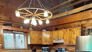 L’intérieur d’une cabane en bois comprend une table à manger, des chaises, un réfrigérateur et un coin cuisine équipé d’une cuisinière et d’un four à micro-ondes.