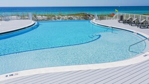 A pool with a 9-inch depth marker, surrounded by a wooden deck, with a view of the ocean and beach in the background. - 1BR Coastal Condo + 3 Pools & Private Beach Access | Magnolia House 107 (Destin)
