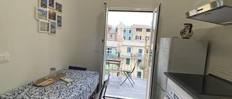 A compact kitchen with a dining area, a view of the city through an open door, and a small balcony with a chair and umbrella.