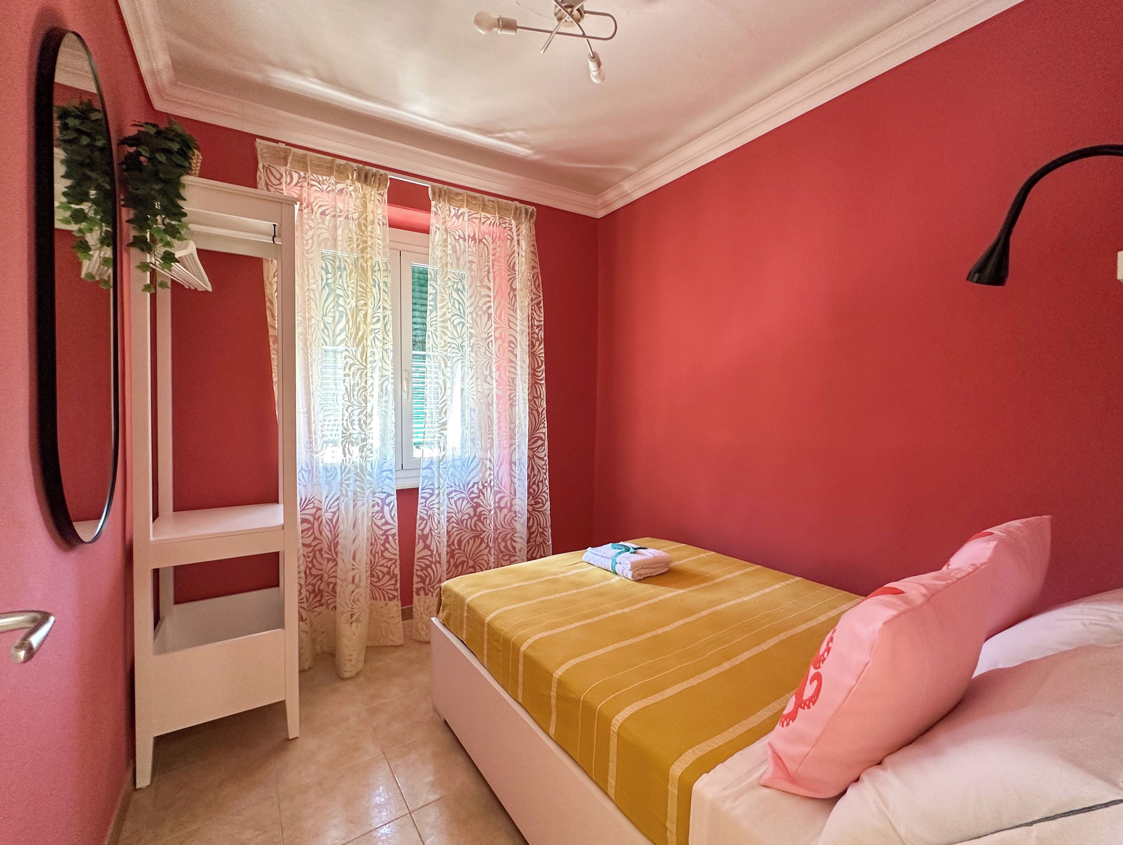 A bedroom with a bed, a white wardrobe, a mirror, and a window with curtains.