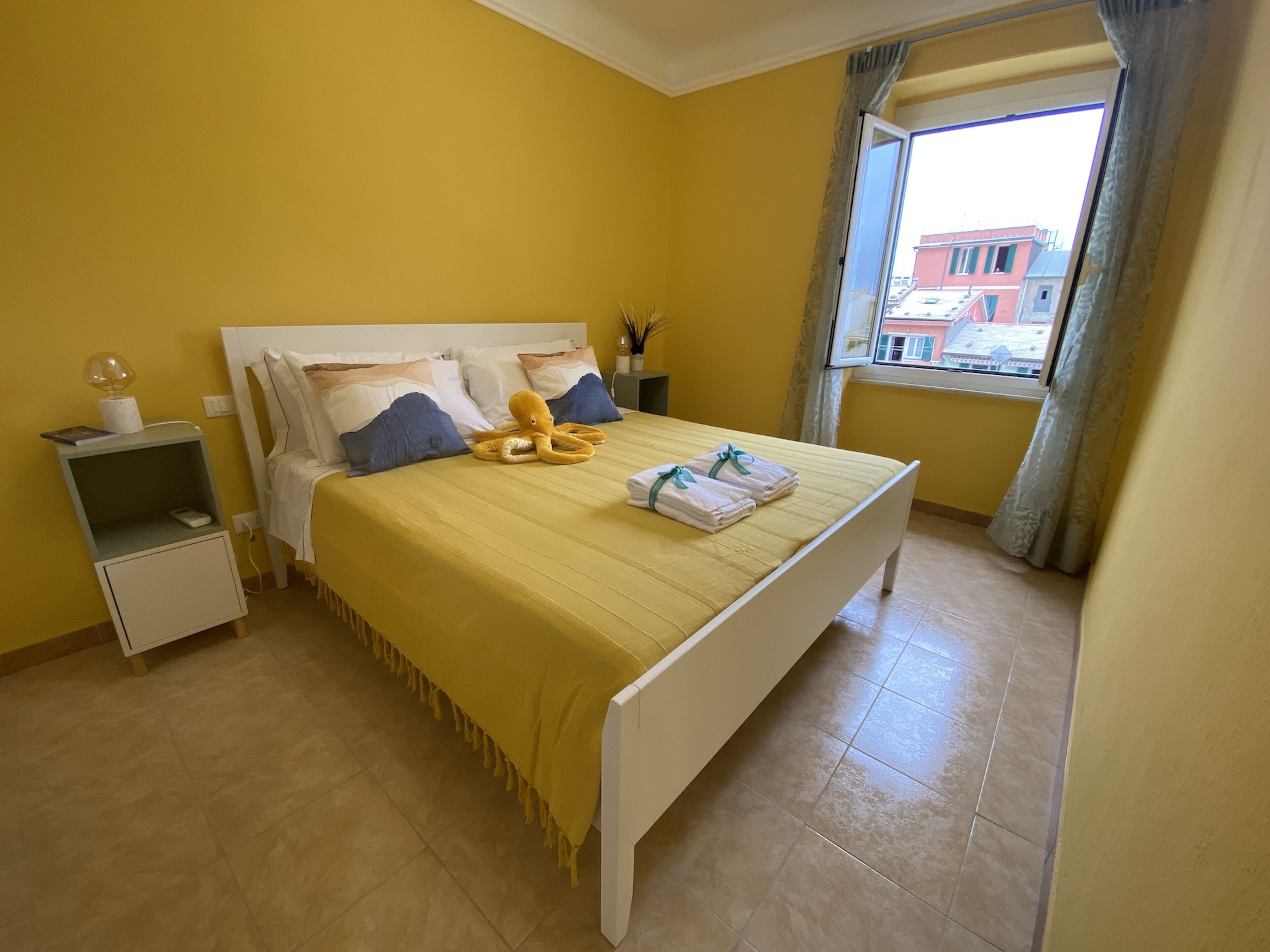 Habitación de hotel con cama, mesita de noche y ventana con vista a edificios.